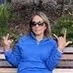 A woman wearing a blue shirt and sunglasses sits on a bench as her Trustpilot reviewer profile picture
