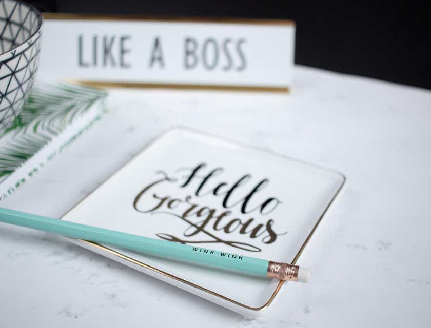 Logo de empoderamiento con un lápiz verde encima que dice “Hello Gorgeous” y un letrero que dice “like a boss” al fondo.