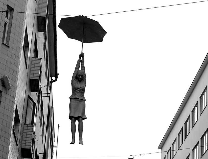 Awangardowa rzeźba kobiety zwisającej z parasolki zawieszonej pomiędzy budynkami.