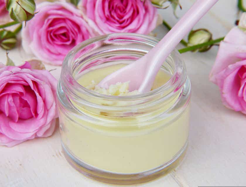 Sebotol body butter kecil dengan sendok merah muda dikelilingi mawar merah muda di bisnis body butter.