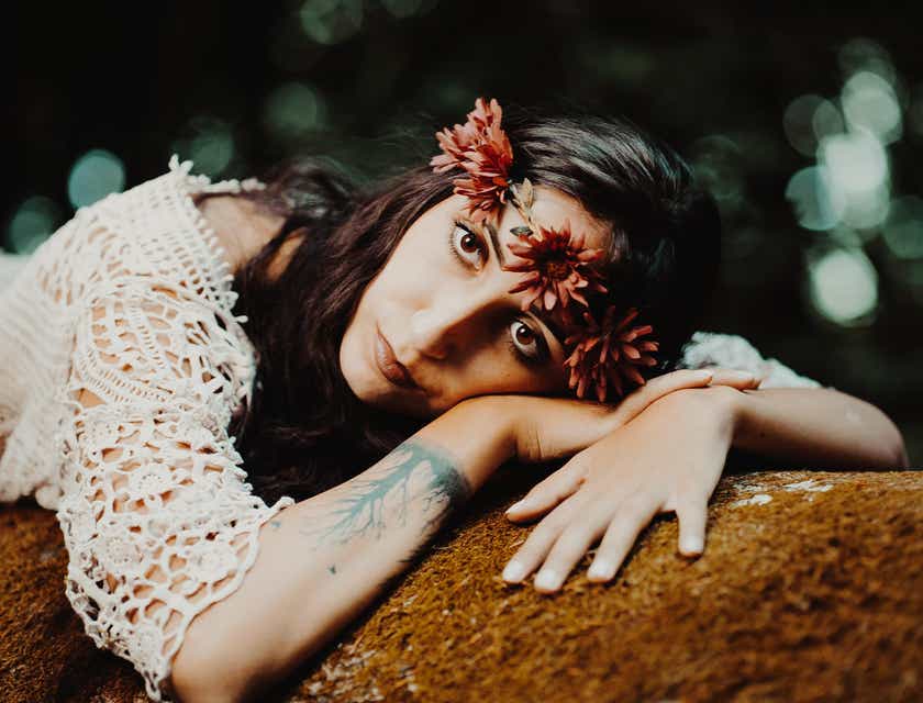 Une femme bohème au poignet tatoué dans un haut crocheté au crochet et avec une couronne de fleurs, allongée sur un rocher.