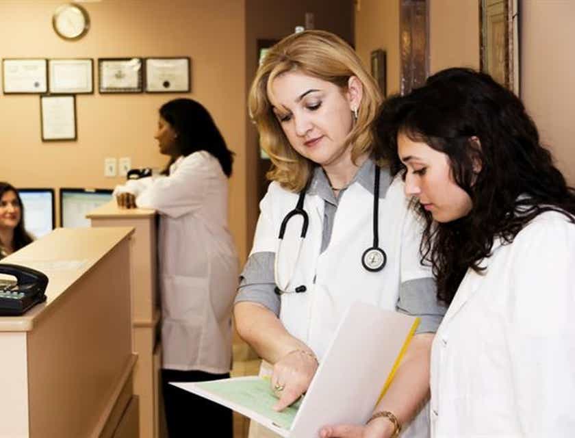 Krankenschwestern schauen während ihrer Schicht in einer Klinik in eine Patientenakte und tauschen sich untereinander aus.