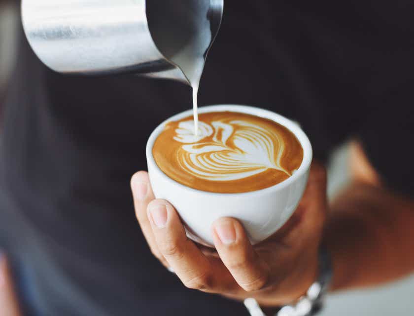 Seorang pria menuangkan busa susu ke dalam secangkir kopi segar.