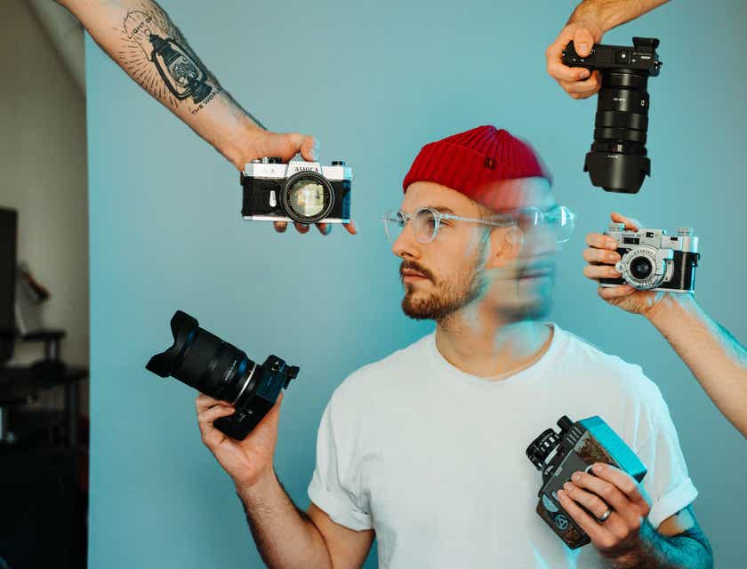 Ein Fotograf steht vor einer blauen Leinwand und ist umgeben von mehreren Kameras, um sich kreativ Szene zu setzen.