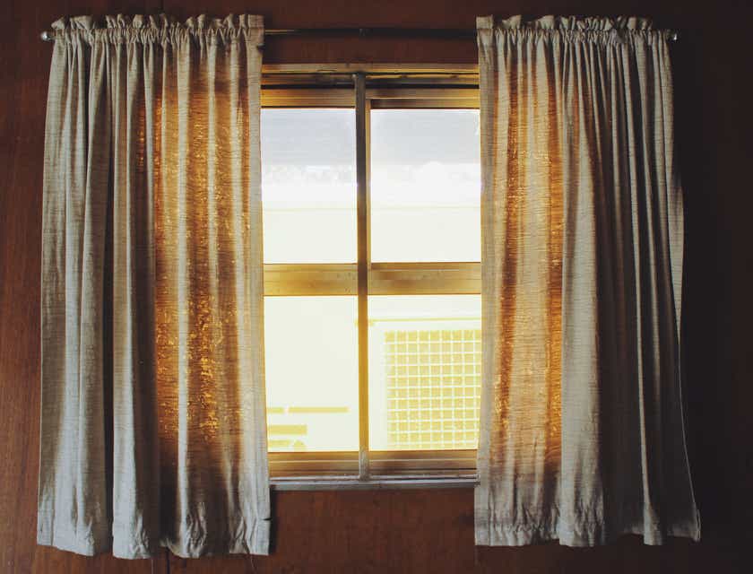 Gorden dan vitrase menutupi jendela besar di ruang tamu sebuah rumah.