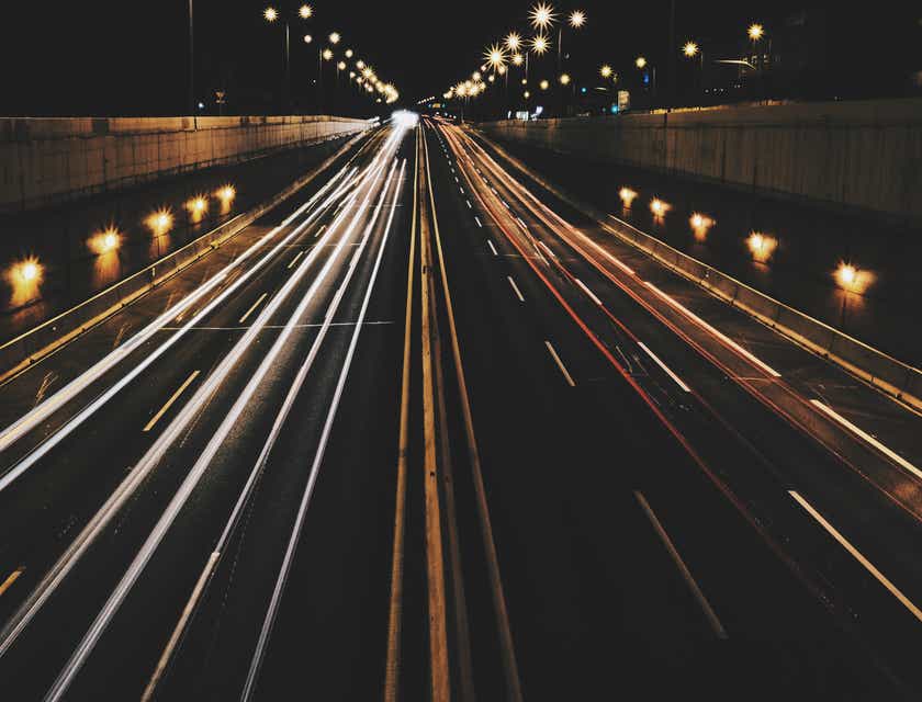 Une route fréquentée, la nuit, avec les phares des voitures qui laissent des traînées lumineuses dynamiques.