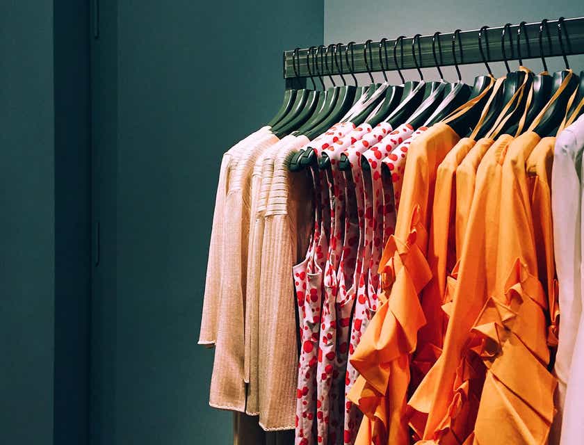 Un rack de chemises et cardigans pour femmes dans un magasin de mode regroupés par couleur et style.