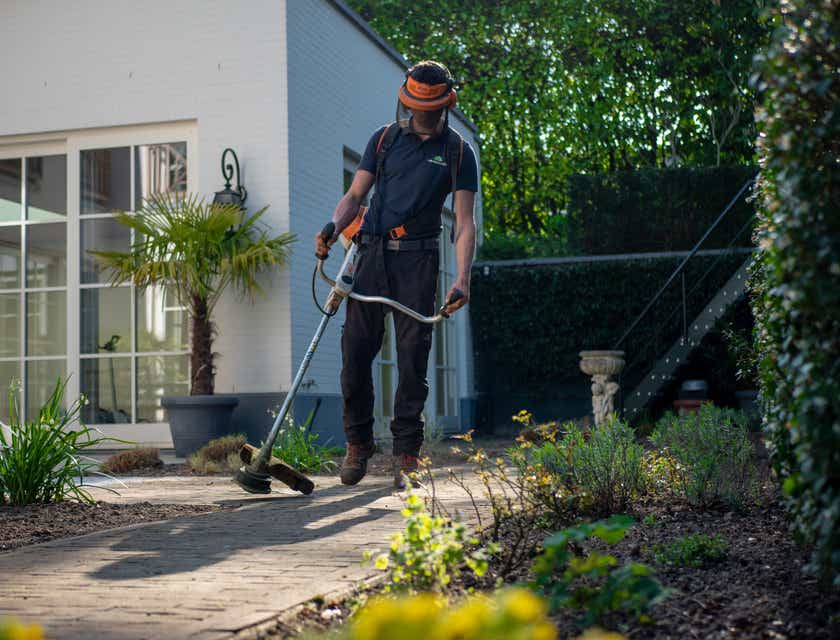 Ein Mann in Arbeitskleidung hält einen Kantenschneider und pflegt einen Garten.