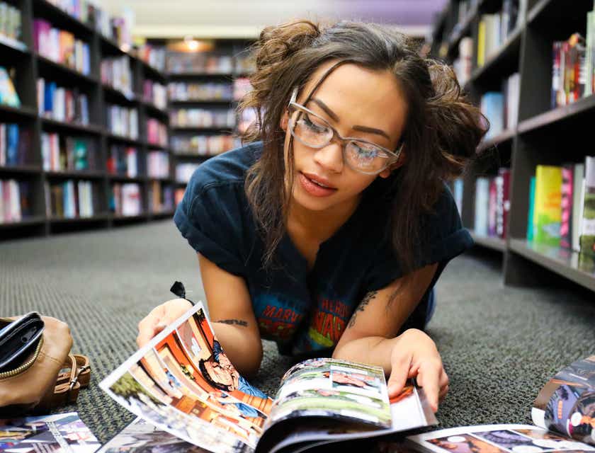 Seorang wanita geek berkacamata yang sedang membaca komik di lantai toko buku.
