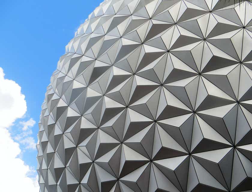 Una vista exterior de un edificio que presenta elementos de diseño geométrico con una franja de cielo azul visible en el fondo en un logo geométrico.