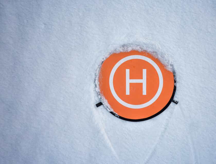 Biała litera „H” na pomarańczowej powierzchni otoczonej śniegiem.