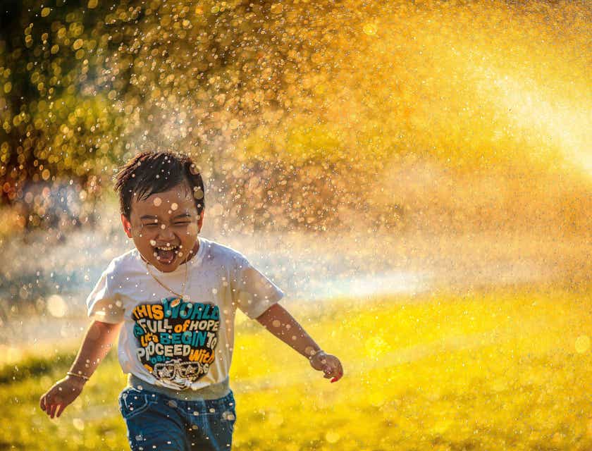 Un bambino felice che corre sotto l'acqua di un irrigatore.