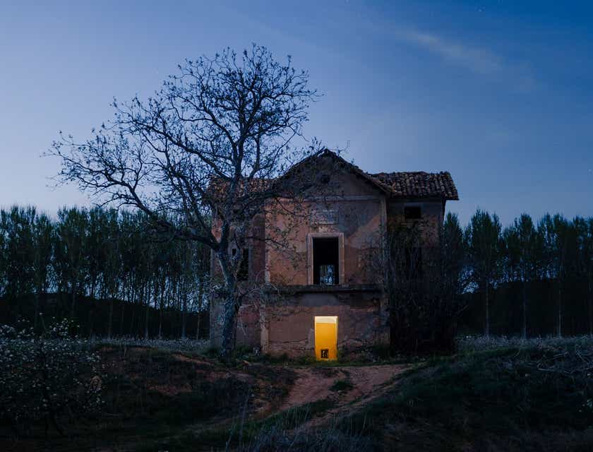 Opuszczony dom strachu oraz bezlistne drzewo w mrokach zapadającej nocy.