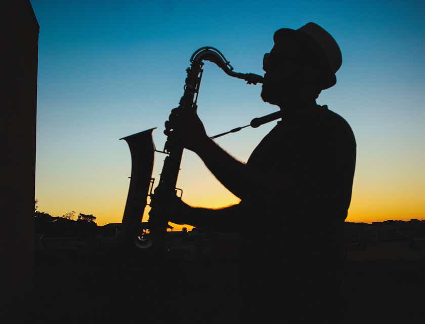 Siluet seorang pria memainkan musik jazz dengan saksofon saat matahari terbenam.