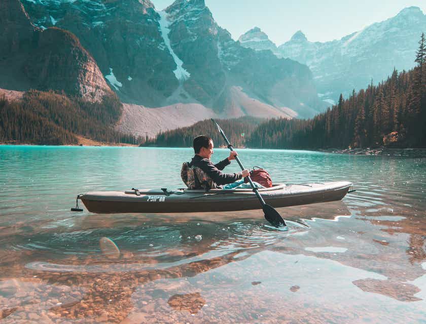Een persoon in een kajak op een meer en tegen een berglandschap als achtergrond.
