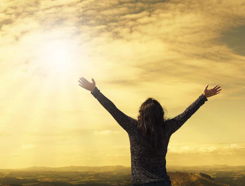 Une femme religieuse avec les bras ouverts vers les cieux et le soleil.
