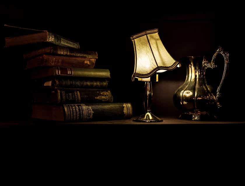 Een stapeltje oude boeken, een schemerlampje en een zilveren koffiepot weerrgegevern in een visueel donkere stijl.