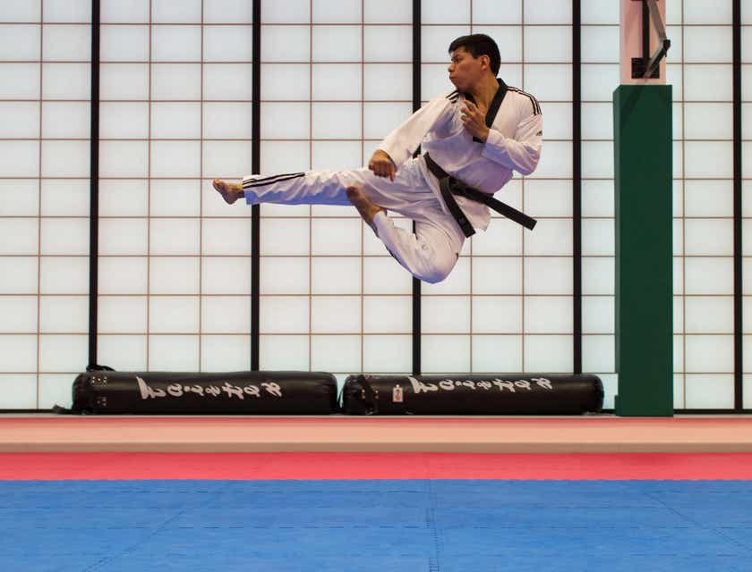 Ein Kampfsportschüler übt auf einer Matte einen Tritt während eines Sprungs.