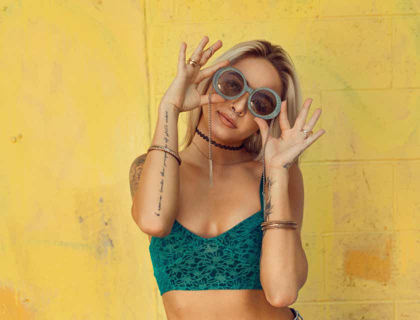 Una donna tatuata che indossa un crop top irriverente e gioca con i suoi occhiali da sole.