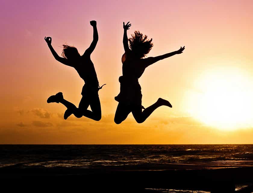 Le silhouette di due persone che saltano di gioia davanti a un tramonto.