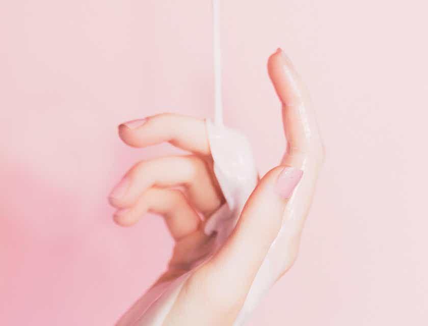Hautmilch wird vor einem pinken Hintergrund auf eine Hand gegossen.
