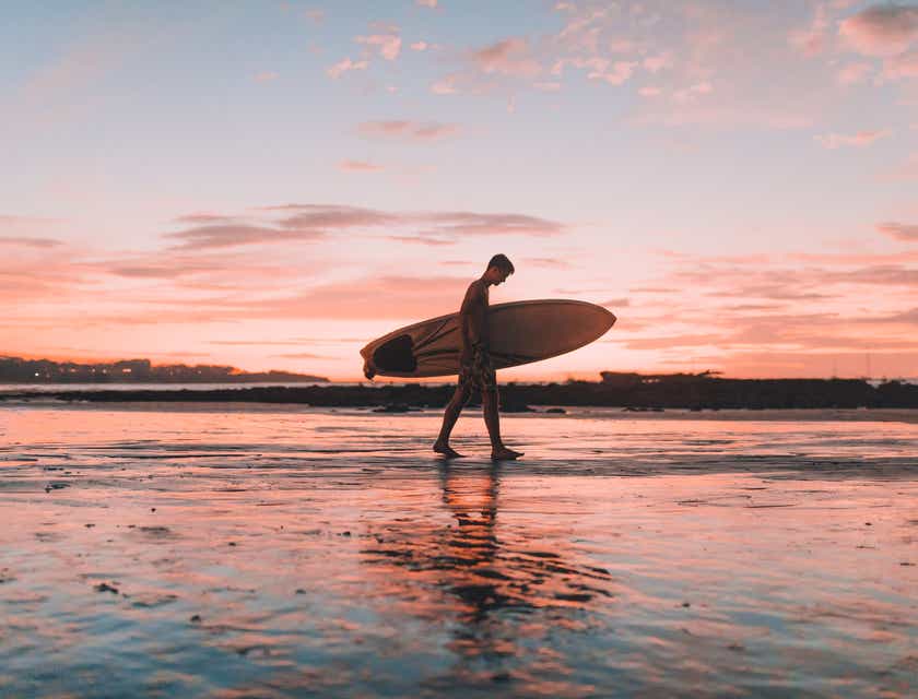 Een surfer die met een surfplank over het strand loopt.
