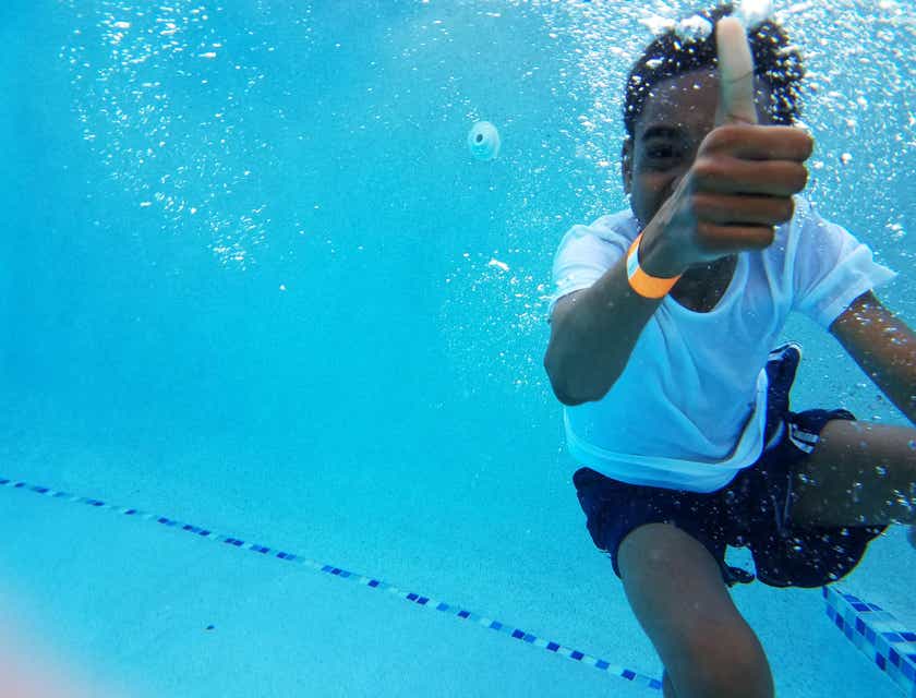 Criança fazendo sinal de positivo embaixo d'água em uma escola de natação.