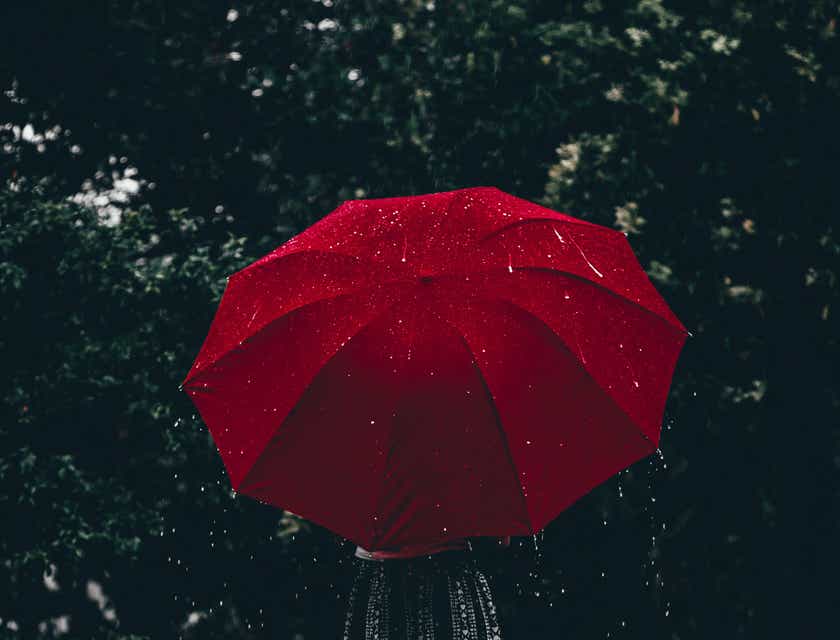 Seseorang memegang payung merah di tengah hujan.