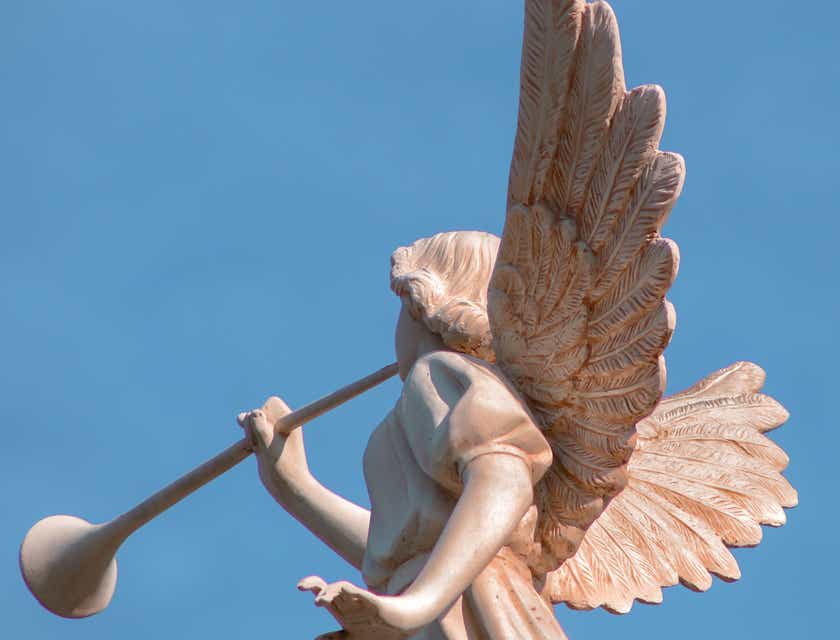 Rzeźba anioła ze skrzydłami oraz trąbką na tle błękitnego nieba.