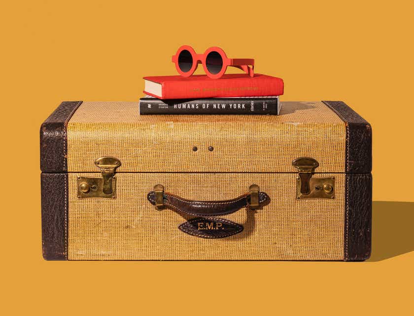 Kacamata hitam dan beberapa buku diletakkan di atas koper seorang traveler.