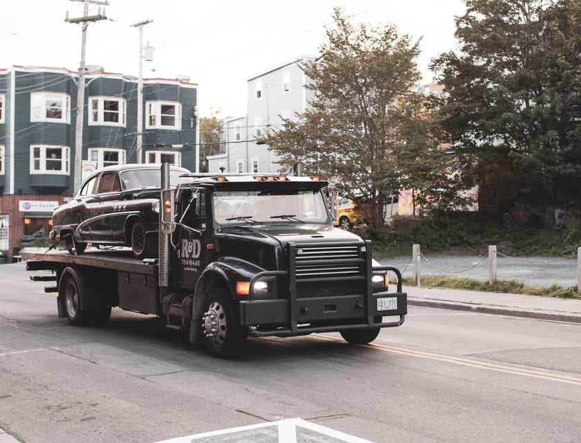 A black tow truck driving down a road.