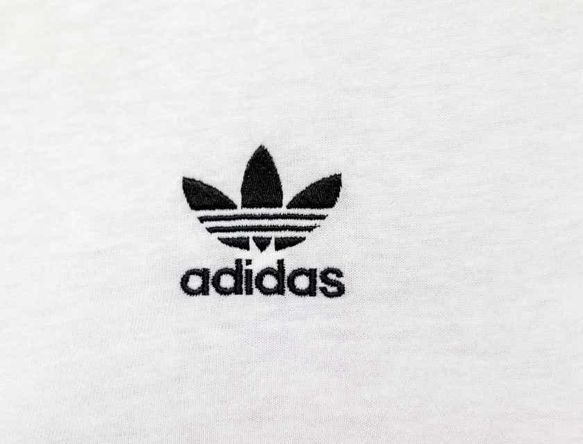Logo Adidas yang terkenal disulam pada kain putih.