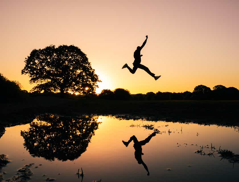 Een actie foto van een persoon die tegen een zonsondergang over een sloot springt.