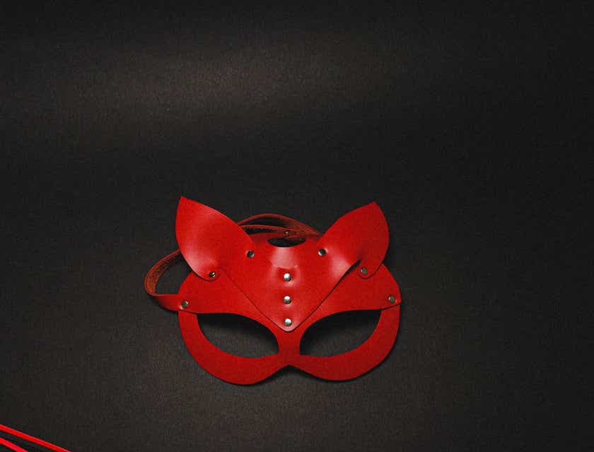 Una máscara y un látigo vendidos en una tienda para adultos sobre un fondo negro.