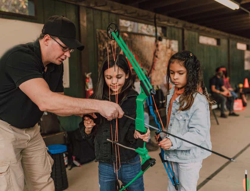 Un uomo che insegna a due bambine a usare l'arco durante una lezione di tiro con l'arco.