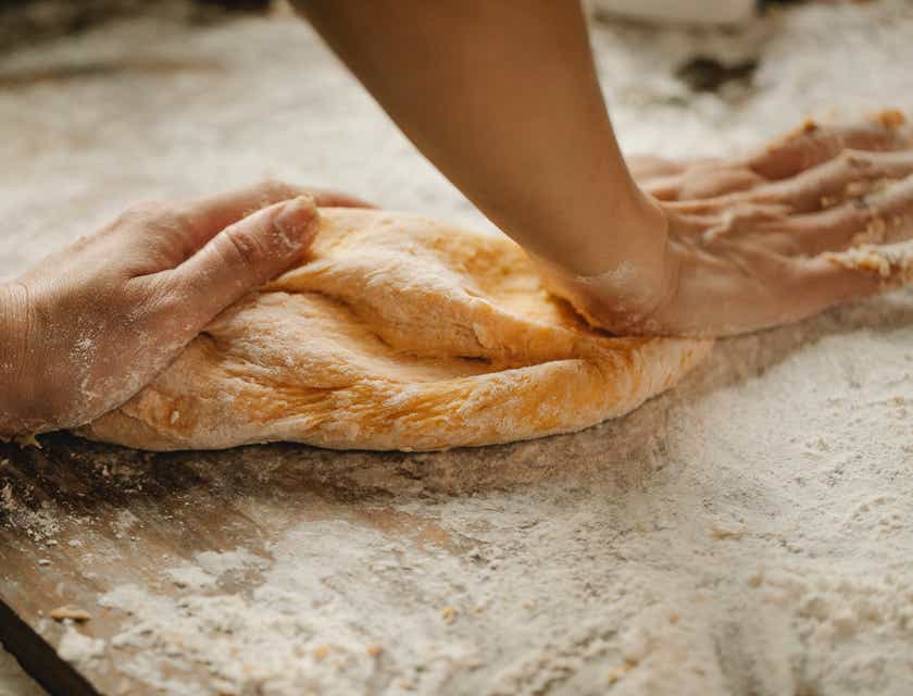 Seorang artisan roti sedang menguleni adonan dengan kedua tangannya.