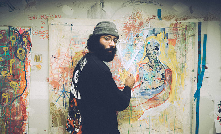 An artist working on a canvas against a wall covered in graffiti.