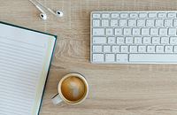 A keyboard, notebook, and earbuds lying on a table near a cup of coffee, ready to be used to write a blog.