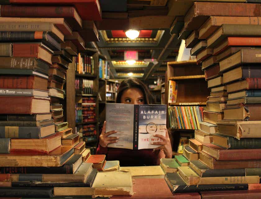 Kobieta pozująca do zdjęcia zza kreatywnie ułożonych książek w księgarni.