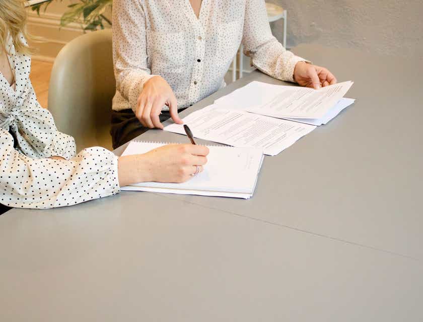 Dos mujeres en un escritorio escribiendo en un papel blanco una propuesta de negocio.