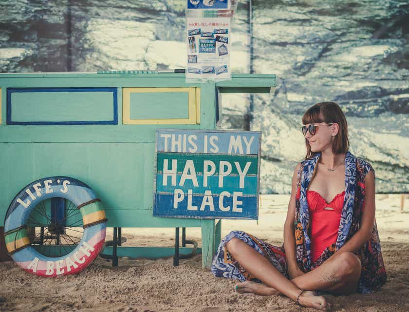 Eine Frau sitzt auf einem Strand neben einem Schild und genießt die Ruhe.
