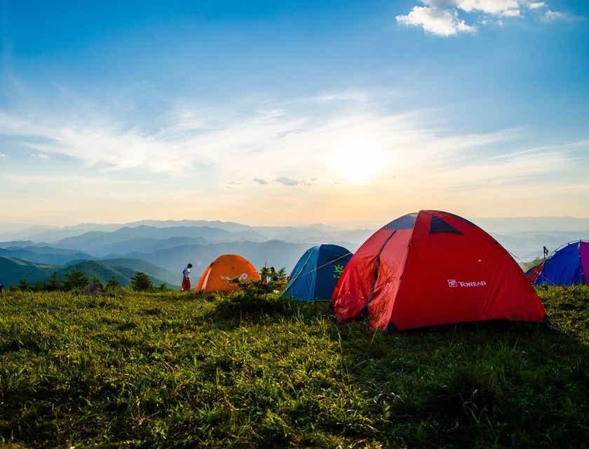 Beberapa tenda berwarna-warni di lokasi camping yang menghadap ke pegunungan.