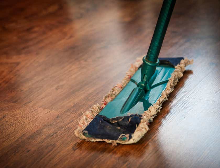 Seorang karyawan cleaning service membersihkan lantai kayu dengan pel.