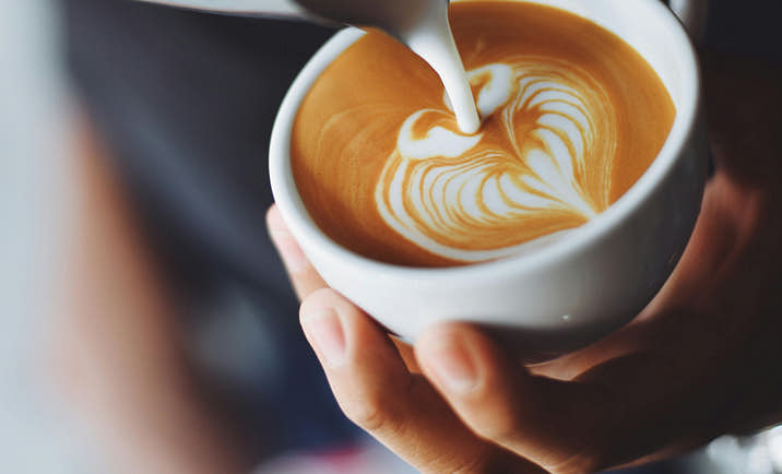 Person pouring milk into a coffee cup.
