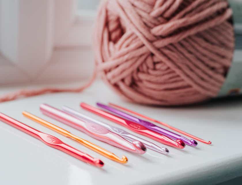 Un gomitolo di filo per uncinetto e una serie di uncinetti colorati sopra un tavolo.