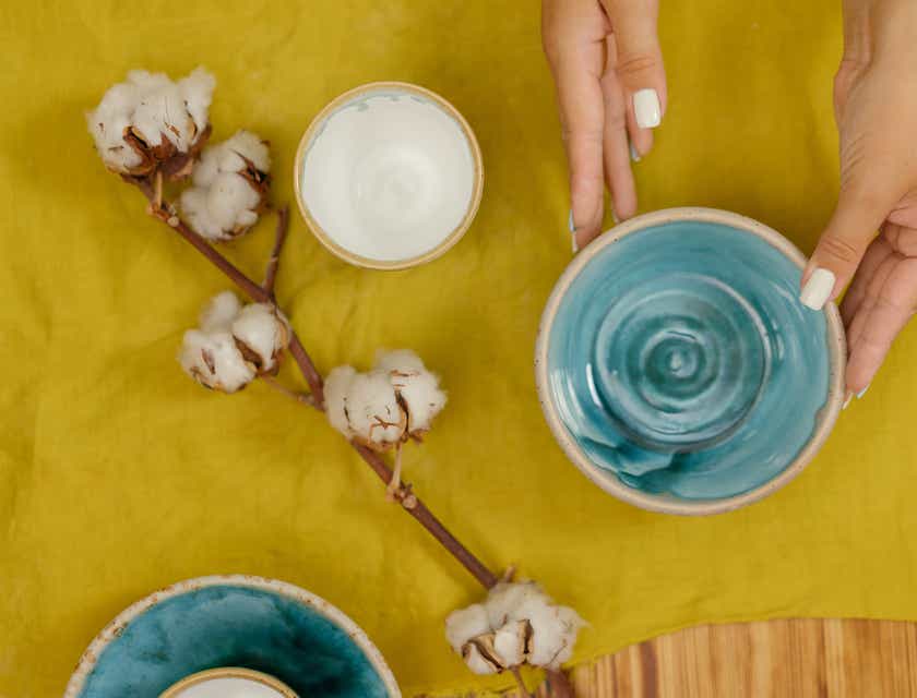 Çanak çömlek olarak kullanılan mavi ve beyaz seramik kaseleri, pamuklu bir yaprağın yanındaki sarı bir masa örtüsüne yerleştiren bir kişi.