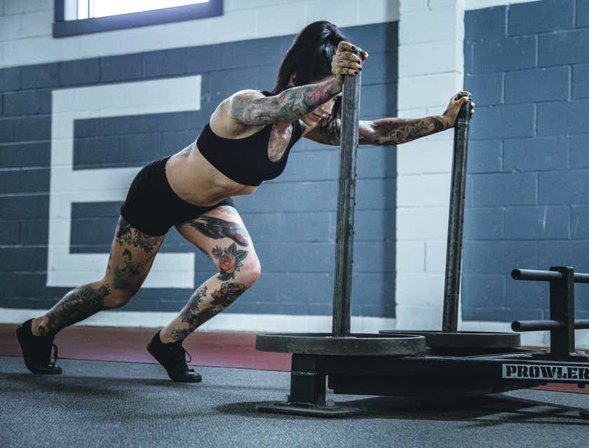 Een getatoeëerde vrouw die trainingsmateriaal vooruit duwt in een CrossFit sportschool.