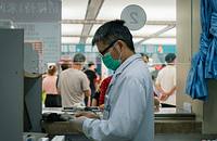 A doctor wearing a white lab coat and face mask sorting through medicines.
