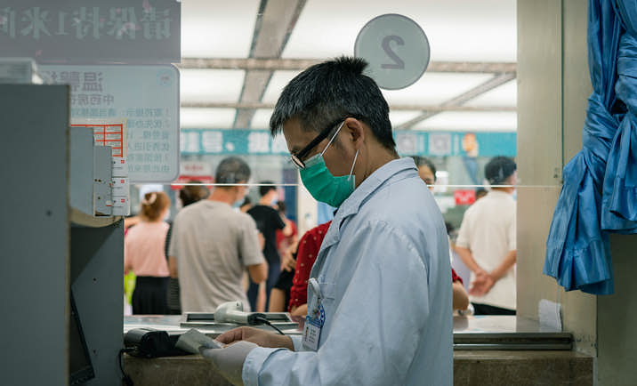A doctor wearing a white lab coat and face mask sorting through medicines.