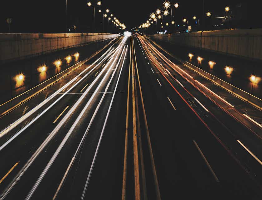 Una strada trafficata, di notte, con i fari delle auto che lasciano delle scie dinamiche di luce.